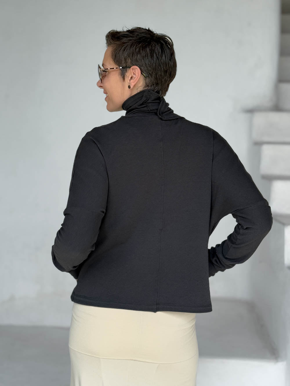 caraucci black bamboo fleece jacket, shown buttoned into a high cowl neck, from the back, with thumbholes and pockets #color_black