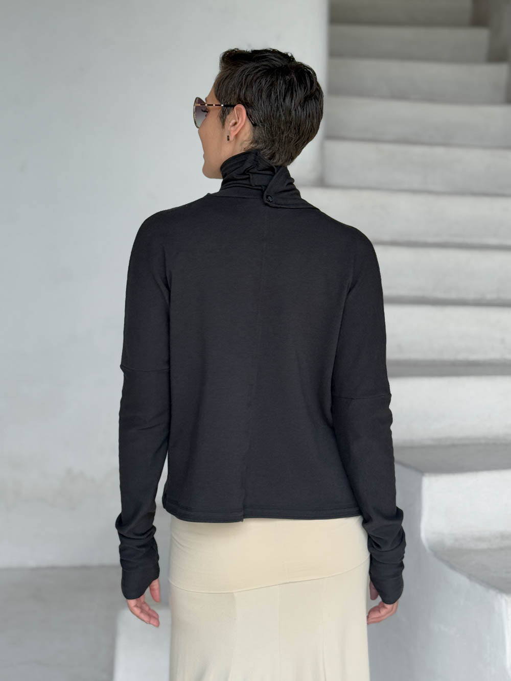 caraucci black bamboo fleece jacket, shown buttoned into a high cowl neck, from the back, with thumbholes and pockets #color_black