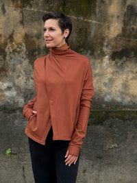 caraucci orange bamboo fleece jacket, shown buttoned into a high cowl neck with thumbholes and pockets #color_copper