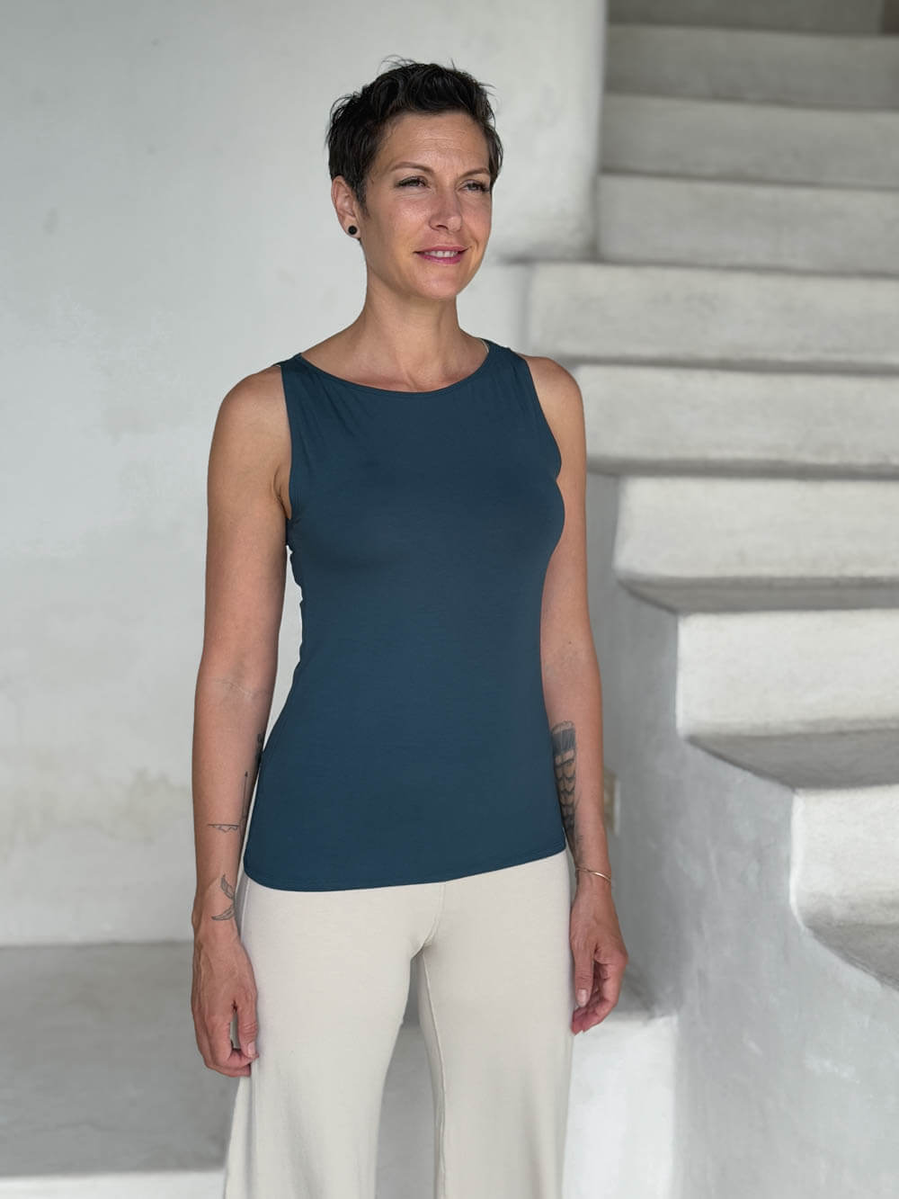 caraucci-woman-wearing-teal-boat-neck-tank-top-in-rayon-jersey-layered-over-cream-pants #color_teal