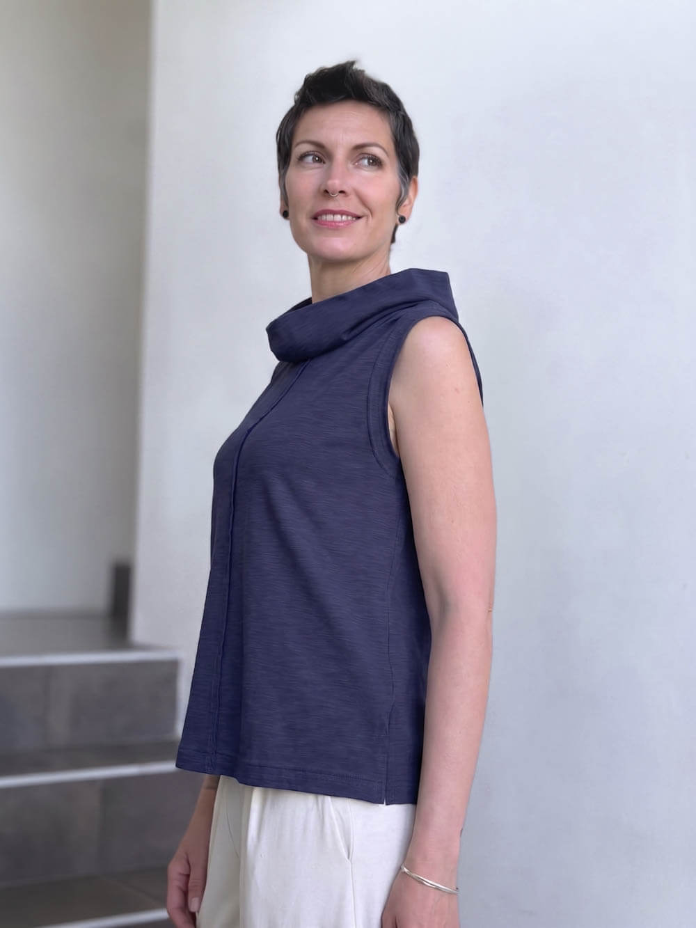 Side view of CARAUCCI Cotton Cowl Neck Tank in denim navy blue with draped neckline, center seam detail and cream skirt. #color_midnight