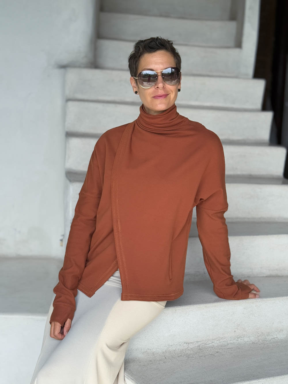caraucci orange bamboo fleece jacket, shown buttoned into a high cowl neck with thumbholes and pockets #color_copper