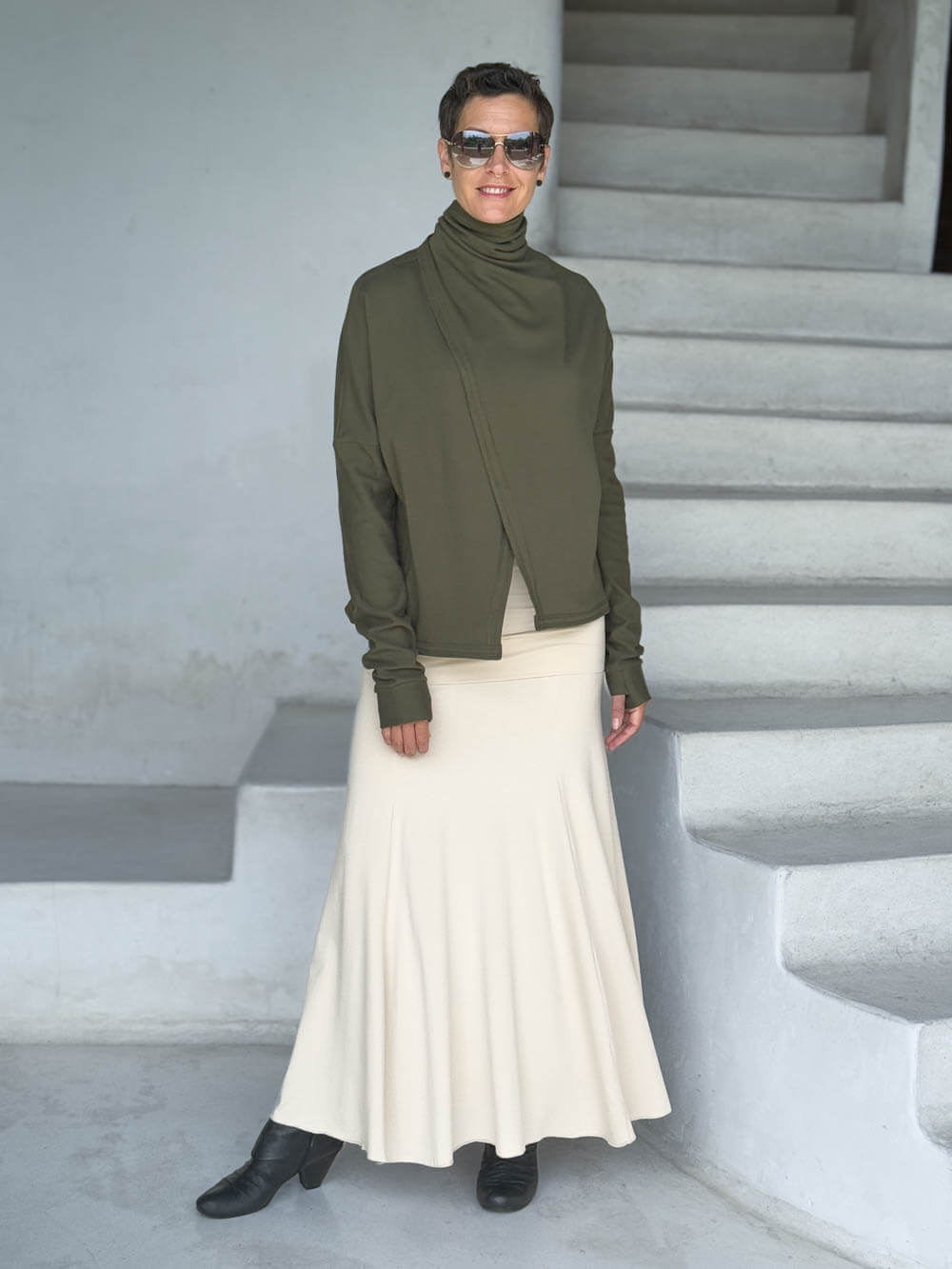 caraucci forest green bamboo fleece jacket, shown buttoned into a high cowl neck with thumbholes and pockets worn with a cream full length skirt #color_forest