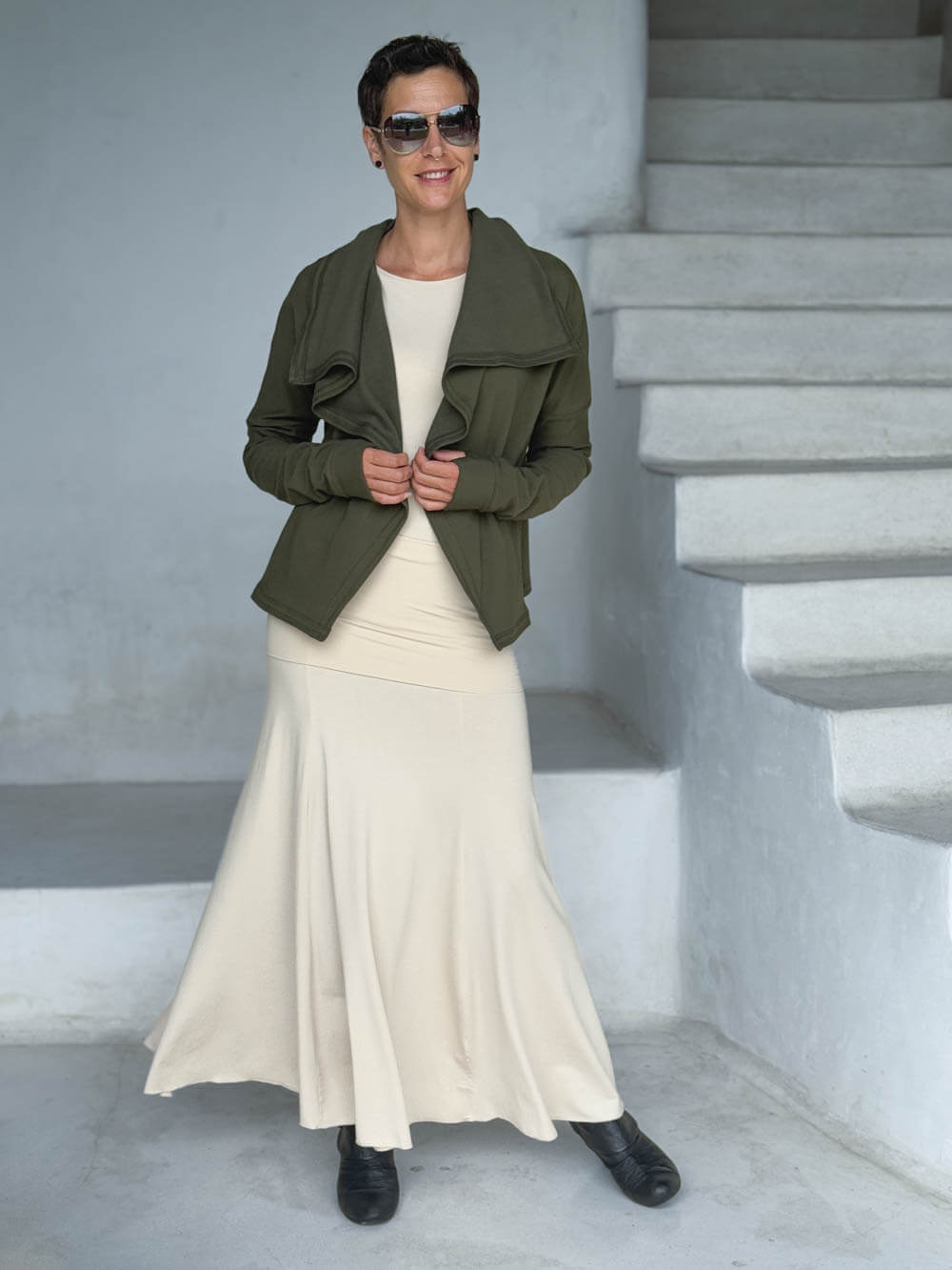 caraucci forest green bamboo fleece jacket, shown buttoned into a high cowl neck with thumbholes and pockets worn with a cream full length skirt #color_forest