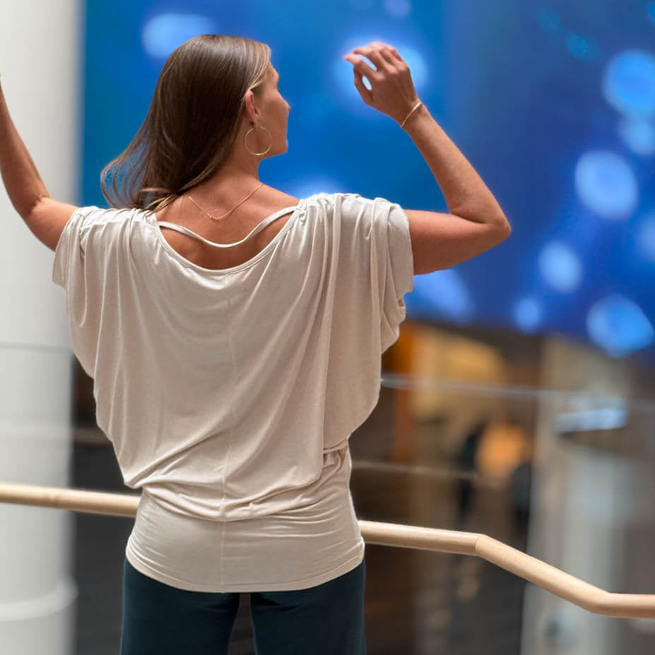 Woman in a white top and blue pants standing on a balcony with a blurred cityscape background